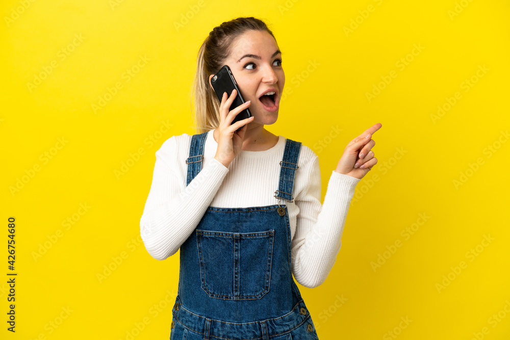 Young woman using mobile phone over isolated yellow background intending to realizes the solution while lifting a finger up Young woman using mobile phone over isolated yellow background intending to realizes the solution while lifting a finger up