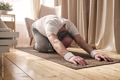 Active senior man doing the child pose while practicing yoga on a mat photo
