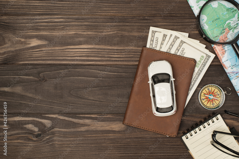 Overhead photo of brown passport wit money dollars cash inside car map magnifier compass notepad and glasses isolated on the wooden backdrop with empty space Overhead photo of brown passport wit money dollars cash inside car map magnifier compass notepad and glasses isolated on the wooden backdrop with empty space