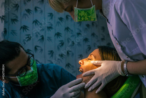 Close up portrait of a beautiful young lady sitting in the dental chair while stomatologist ( dentist ) with hands in sterile gloves is fixing her teeth.