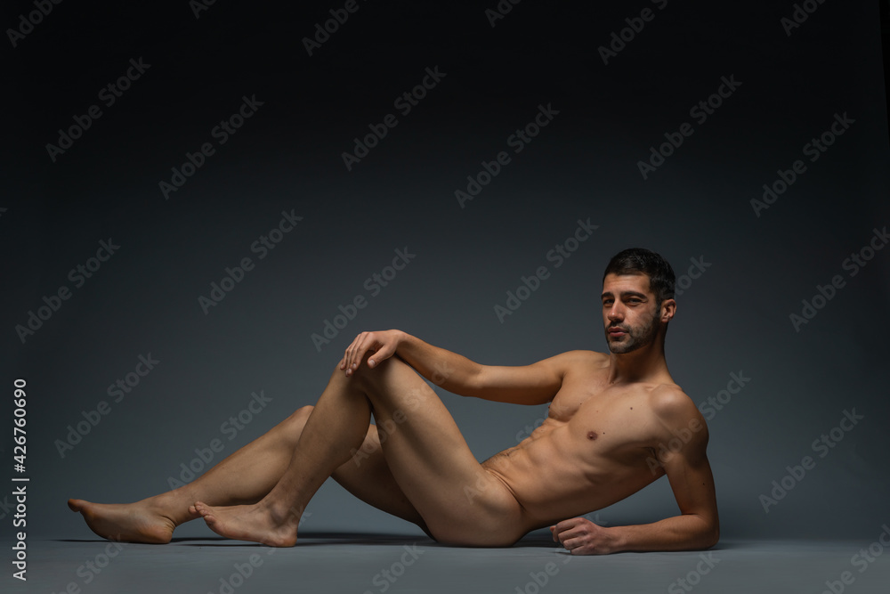 Fashion nude photo of a male model with seductive figure lying isolated on the floor in a studio Fashion nude photo of a male model with seductive figure lying isolated on the floor in a studio