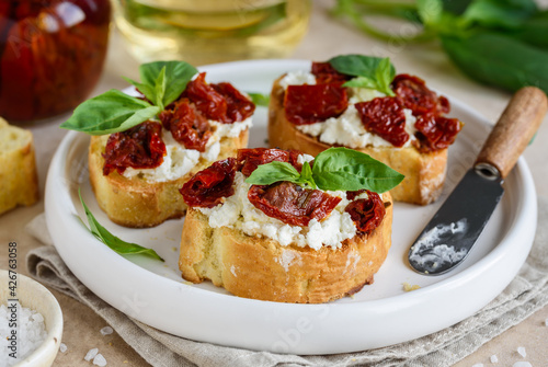 Bruschetta with sun dried tomatoes, cream cheese and basil on a white plate. Italian appetizer. 
 Selective focus