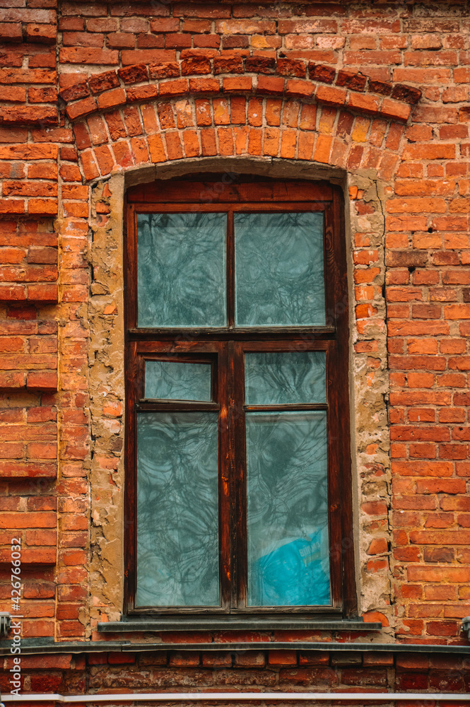 An old window in a brick house. The building is made of red brick. Brown wooden frames. Historical building. Design and pattern template. Patterns made of old bricks. An old window in a brick house. The building is made of red brick. Brown wooden frames. Historical building. Design and pattern template. Patterns made of old bricks.
