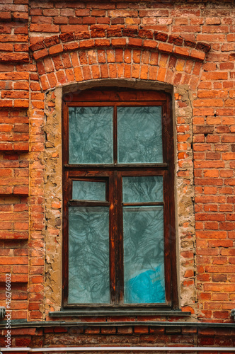 An old window in a brick house. The building is made of red brick. Brown wooden frames. Historical building. Design and pattern template. Patterns made of old bricks.