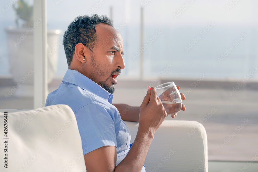 African man holding pill glass of water at home African man holding pill glass of water at home