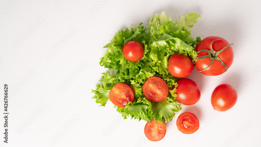 Juicy and ripe cherry tomatoes and green fresh lettuce on a white background. Top view. Copy space - obrazy, fototapety, plakaty 