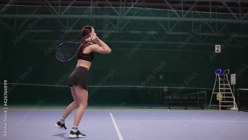 young woman is playing tennis on indoor court, striking ball by tennis racquet, running over area, slow motion young woman is playing tennis on indoor court, striking ball by tennis racquet, running over area, slow motion