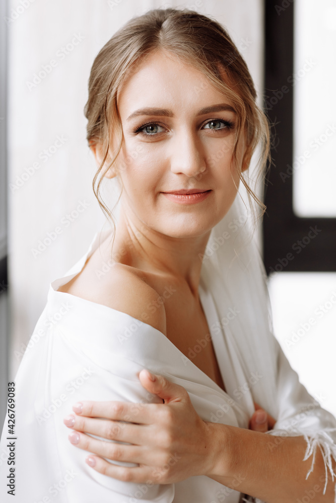 Morning of bride. Gorgeous bride. beautiful woman with long hair in a white robe at the window. the morning of the bride before the wedding.Natural beauty and professional make-up. skin care products Morning of bride. Gorgeous bride. beautiful woman with long hair in a white robe at the window. the morning of the bride before the wedding.Natural beauty and professional make-up. skin care products