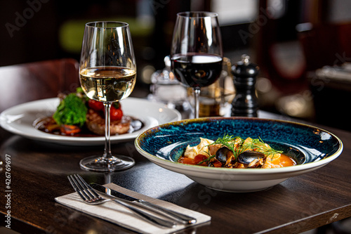 Фотография A close up of a plate of food and two glasses of wine on a table in a restaurant