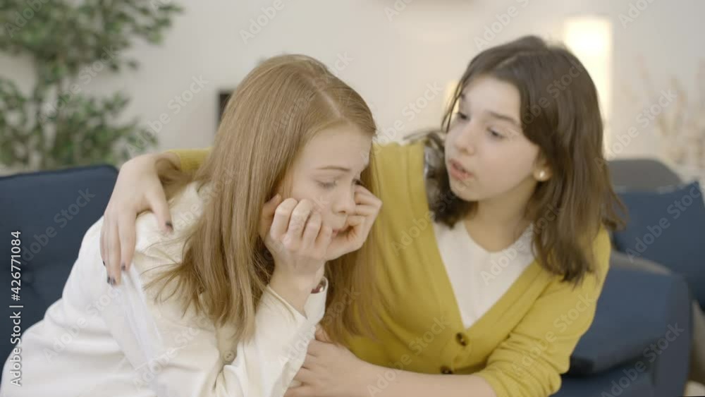 Teenage girl comforting her crying broken-hearted female friend, sitting on sofa Teenage girl comforting her crying broken-hearted female friend, sitting on sofa