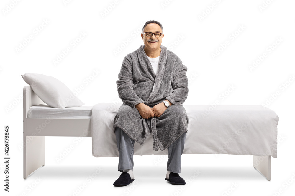 Mature man in pajamas and a robe sitting on a bed