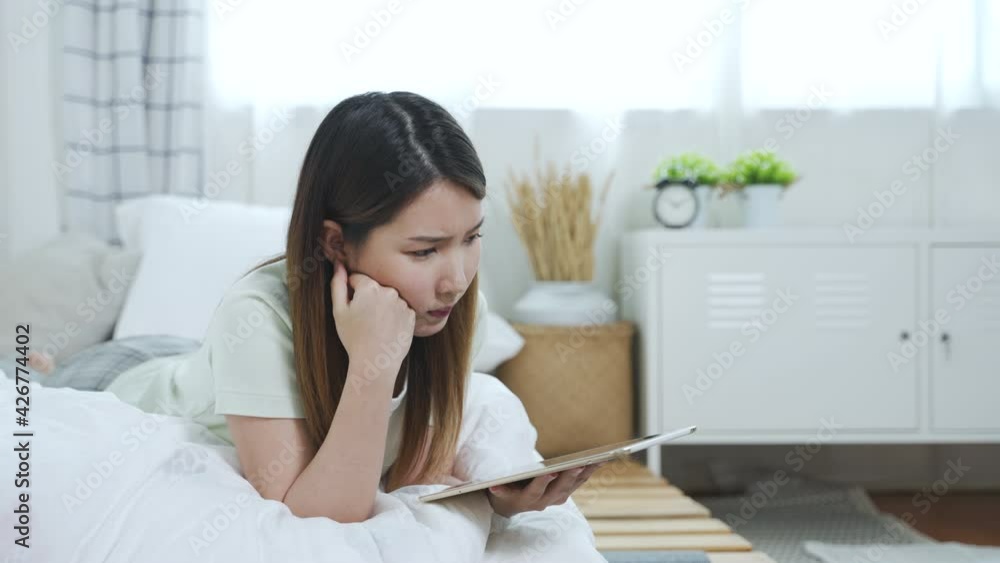 Thoughtful concerned Asian woman using tablet thinking something to solve the problems, imagining in mind to make the decision for her job in bedroom Thoughtful concerned Asian woman using tablet thinking something to solve the problems, imagining in mind to make the decision for her job in bedroom