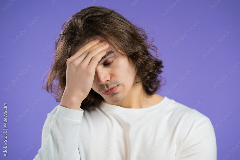 Young man having headache, studio portrait. Guy putting hands on head, isolated on violet background. Concept of problems, medicine, illness