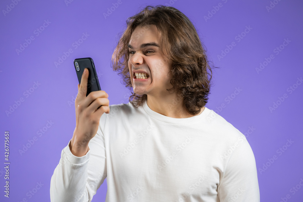 Angry man in white t-shirt screaming down his mobile phone. Stressed and depressed guy on violet background. Angry man in white t-shirt screaming down his mobile phone. Stressed and depressed guy on violet background.
