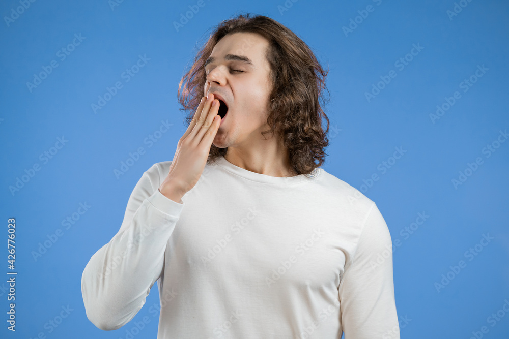 Tired sleepy man yawns. Lazy guy with long hairdo showing emotion of very boring, uninteresting,. Blue studio background. Tired sleepy man yawns. Lazy guy with long hairdo showing emotion of very boring, uninteresting,. Blue studio background.