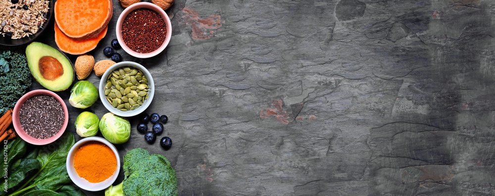 Group of healthy food ingredients. Top view side border on a slate banner background. Copy space. Super food concept with green vegetables, berries, whole grains, seeds, spices and nutritious items. Group of healthy food ingredients. Top view side border on a slate banner background. Copy space. Super food concept with green vegetables, berries, whole grains, seeds, spices and nutritious items.