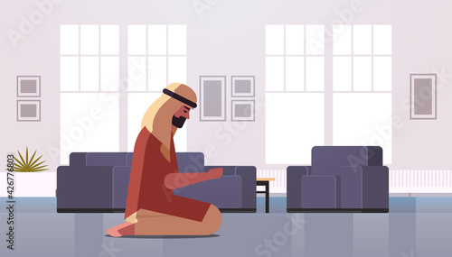 religious muslim man kneeling and praying at home ramadan kareem holy month religion concept modern living room interior full length horizontal