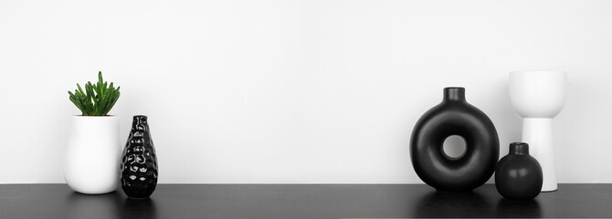 Modern black and white home decor and plants on a shelf. Black shelf against a white wall. Banner with copy space.