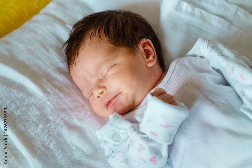 Close up on newborn happy caucasian baby sleeping in bed at home on first day of her life - cute little infant girl sleep peacefully Close up on newborn happy caucasian baby sleeping in bed at home on first day of her life - cute little infant girl sleep peacefully