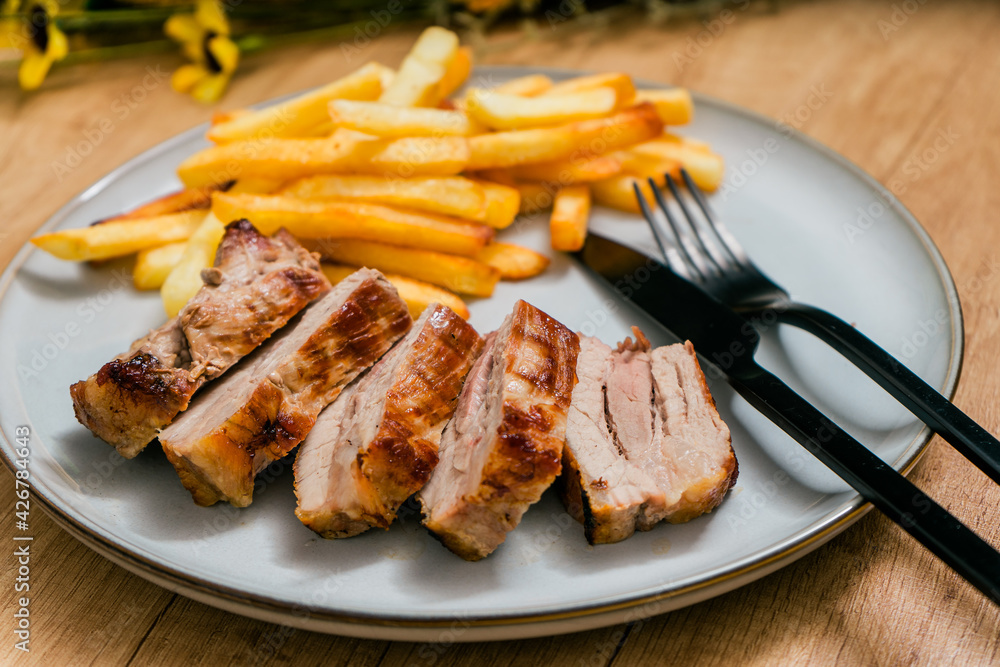 Grilled pork breast cut into strips on a plate with french fries. Grilled pork breast cut into strips on a plate with french fries.