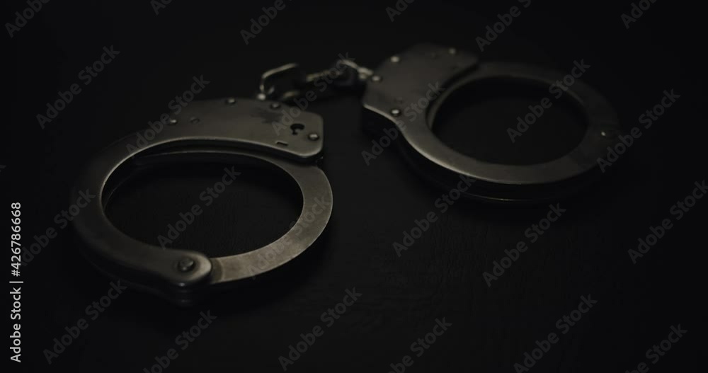 Pair of handcuffs used by law enforcement to arrest criminals, lit in red and blue flashing police lights. Justice or catching a guilty criminal concept. Pair of handcuffs used by law enforcement to arrest criminals, lit in red and blue flashing police lights. Justice or catching a guilty criminal concept.