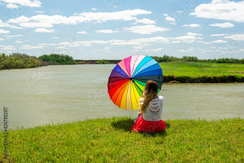 a multi-colored umbrella on the bank of the river in the hands of a girl