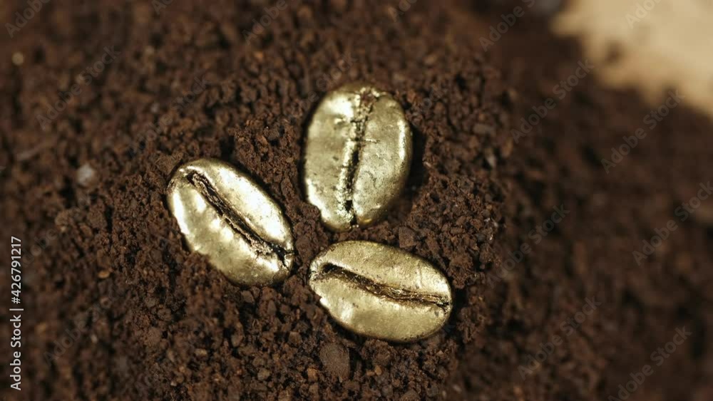 Golden coffee beans. Three roasted gold coffee beans lie on the ground coffee and slowly rotate. 4K Golden coffee beans. Three roasted gold coffee beans lie on the ground coffee and slowly rotate. 4K