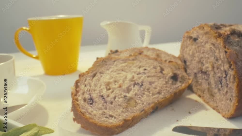 Zoom out of sliced rye raisin bread to the whole white dinner table on which there is a cup of tea, bowl of salad, white milk jug, yellow mug and some pack of honey on the front. Close-up in focus, zo Zoom out of sliced rye raisin bread to the whole white dinner table on which there is a cup of tea, bowl of salad, white milk jug, yellow mug and some pack of honey on the front. Close-up in focus, zo