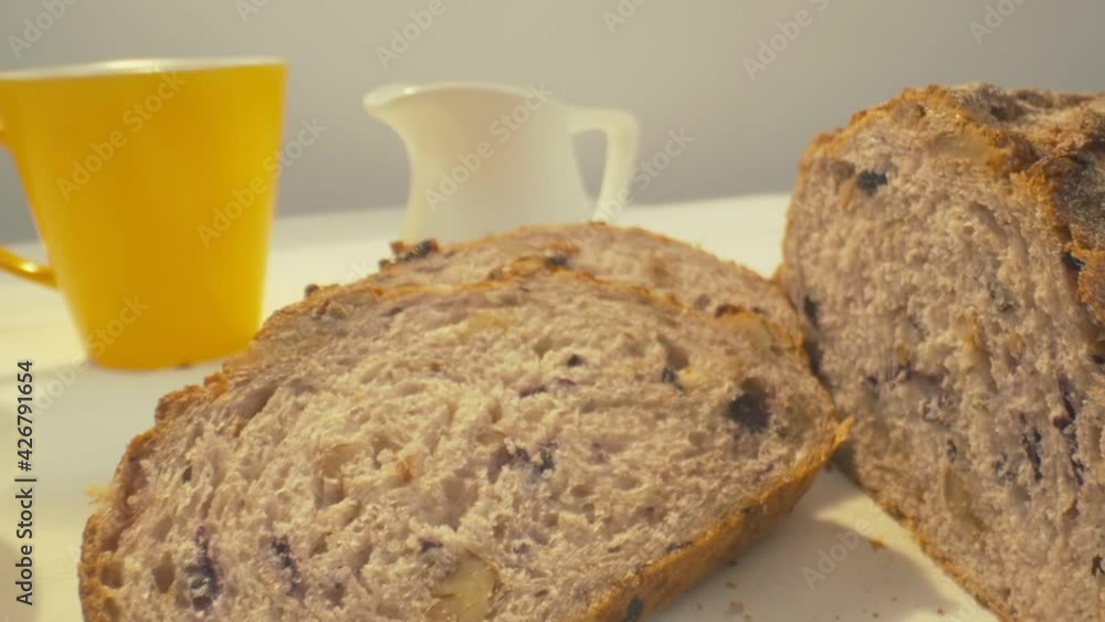 Zoom out of sliced rye raisin bread to the whole white dinner table on which there is a cup of tea, bowl of salad, white milk jug, yellow mug and some pack of honey on the front. Close-up in focus, zo Zoom out of sliced rye raisin bread to the whole white dinner table on which there is a cup of tea, bowl of salad, white milk jug, yellow mug and some pack of honey on the front. Close-up in focus, zo