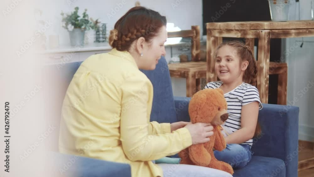 mom plays with her daughter at home in a toy teddy bear. happy family kid dream stay home concept. fun mom plays with daughter on the couch sitting with toy teddy bear mom plays with her daughter at home in a toy teddy bear. happy family kid dream stay home concept. fun mom plays with daughter on the couch sitting with toy teddy bear