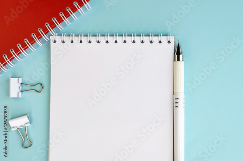 An open notebook with a white blank sheet and a pen on a blue background. Working space