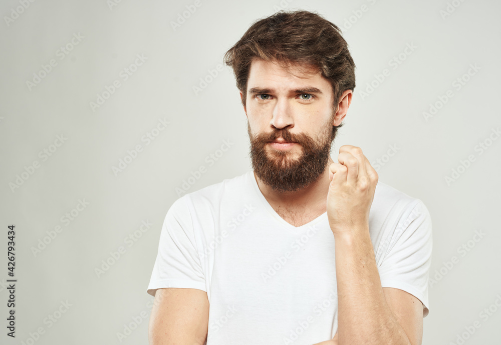 Fototapeta premium Nice guy with a beard in a white T-shirt on a light background cropped view of a sad face