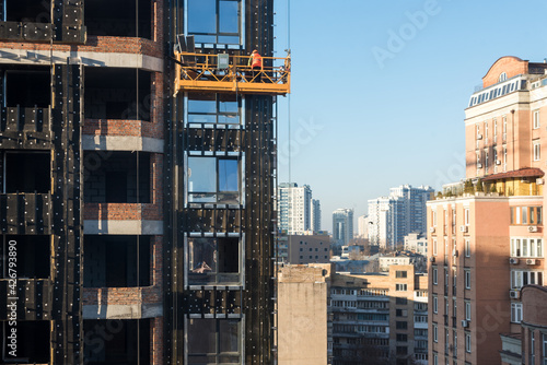 High rise construction work. Construction site workers in cradles working with facade. Suspended cradle for builders to work outside the skyscraper. Building construction