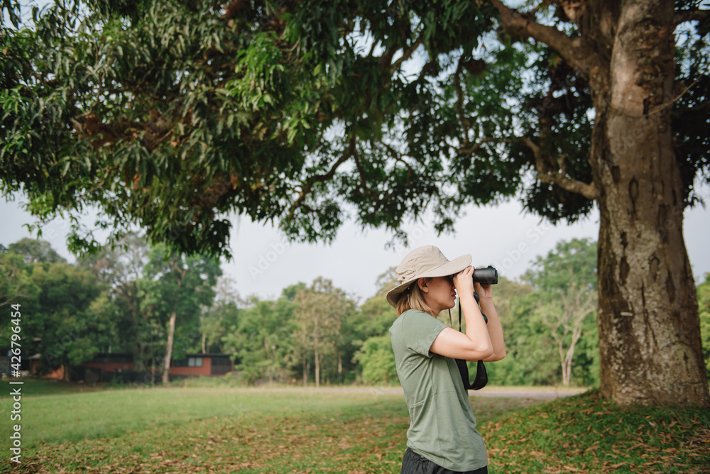 Young asian girl with hiking hat looks through binoculars between a travel.
