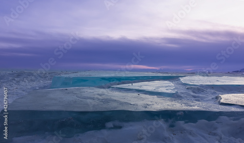 Large flat ice hummocks lie on the surface of the frozen lake. Turquoise ice against the lilac evening sky. Baikal in winter.