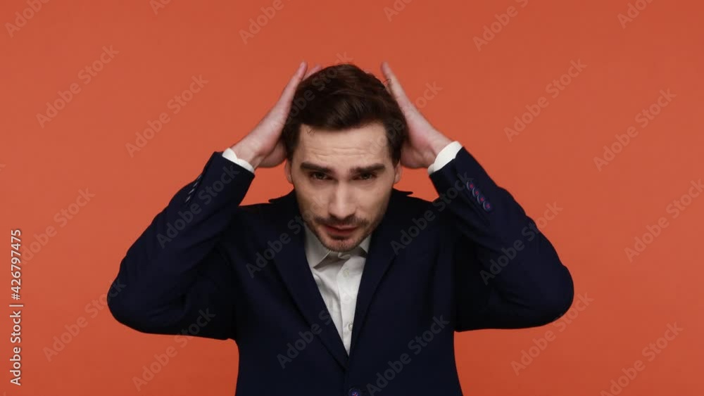 Handsome young man in black business suit looks at himself in mirror and straightens his hair preparing for working day, tidies up and freshen himself. Indoor studio shot isolated on orange background Handsome young man in black business suit looks at himself in mirror and straightens his hair preparing for working day, tidies up and freshen himself. Indoor studio shot isolated on orange background