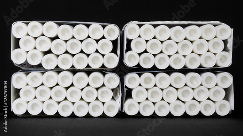 Tablou pe pânză Many cigarettes with white filters with built-in innovative air chambers, lie in four packs against a dark background