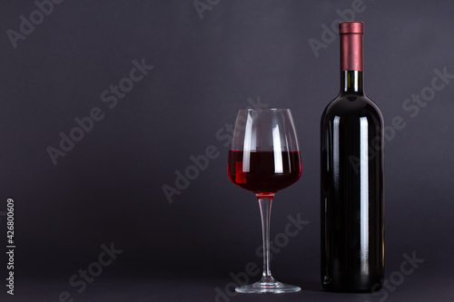 Sealed bottle of red wine and glass on a lilac background.With space for text.