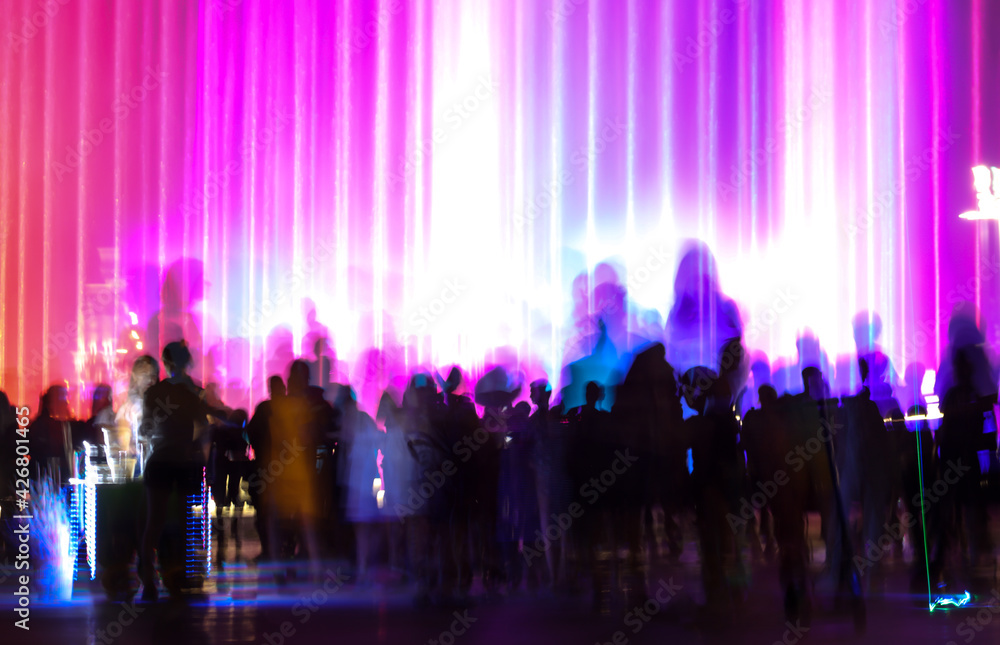 Silhouettes of people in motion near a colored fountain at night.
