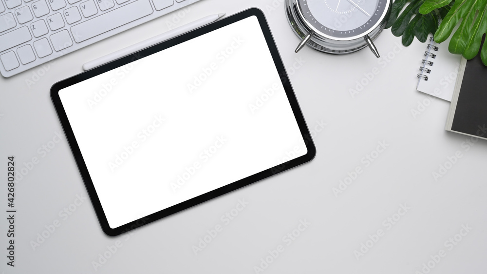 Above view of digital tablet with empty screen, notebook and key board on white office desk. Above view of digital tablet with empty screen, notebook and key board on white office desk.