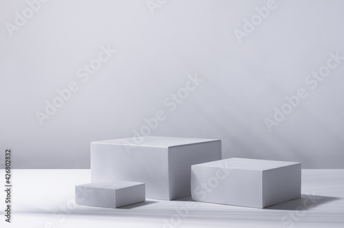 Elegant summer abstract white podiums in sunlight with shadow palm leaf on white background for product display. Simple modern geometric design.