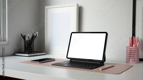Feminine workplace with computer tablet, smart phone, pencil holder and empty frame on white table. © Prathankarnpap