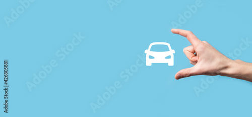 Male hand holding car auto icon on blue background. Wide banner composition.Car automobile insurance and collision damage waiver concepts