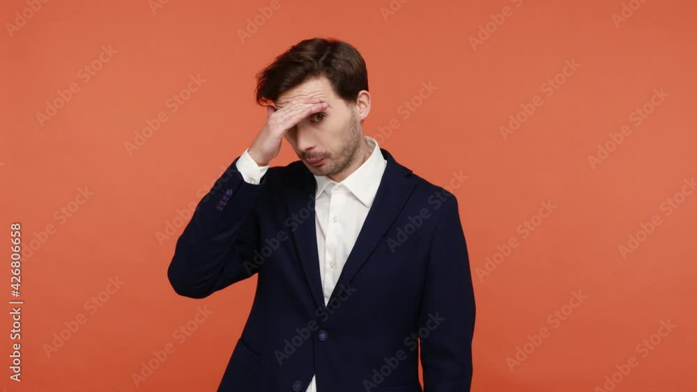 Caucasian young curious bearded man in black suit closing eyes with palm, spying, cautiously watching forbidden secret, taking glance. Indoor studio shot isolated on orange background Caucasian young curious bearded man in black suit closing eyes with palm, spying, cautiously watching forbidden secret, taking glance. Indoor studio shot isolated on orange background