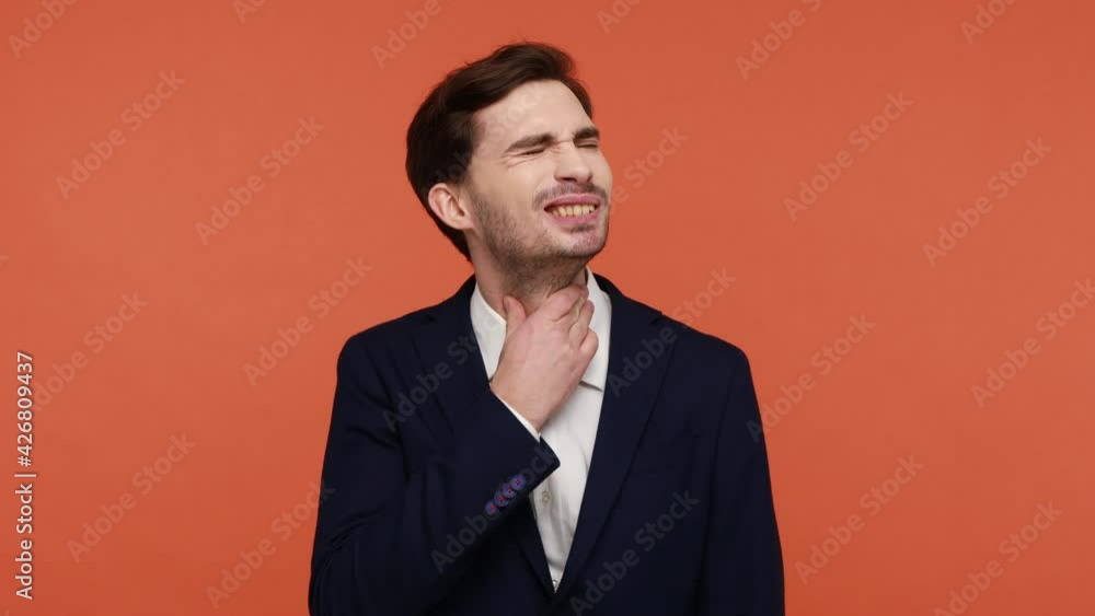 Throat pain. Young man in suit rubbing his neck and suffering from pain, has sore throat or tonsils inflammation, being unhealthy, feels bad. Indoor studio shot isolated on orange background Throat pain. Young man in suit rubbing his neck and suffering from pain, has sore throat or tonsils inflammation, being unhealthy, feels bad. Indoor studio shot isolated on orange background