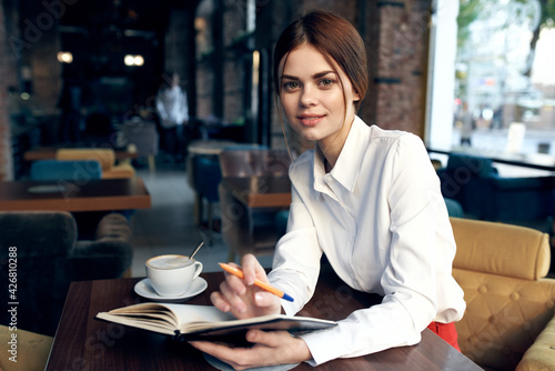 a woman in a shirt with a notebook and a pen in her hand sits at a table in a restaurant on an upholstered chair