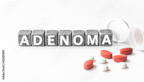 word ADENOMA is made of stone cubes on a white background with pills. medical concept of treatment, prevention and side effects. benign growth in organs epithelial cells