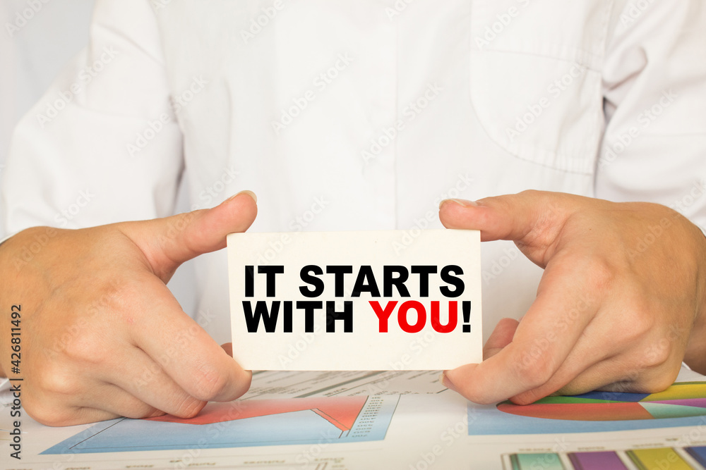 a man in the office holds a card with text IT STARTS WITH YOU . business concept a man in the office holds a card with text IT STARTS WITH YOU . business concept