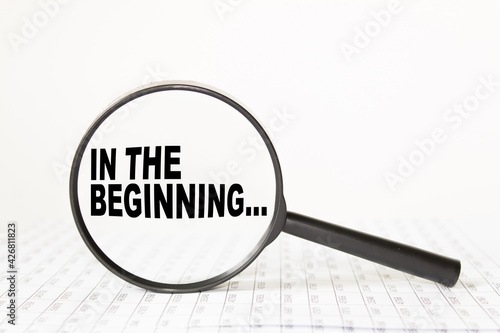 words IN THE BEGINNING in a magnifying glass on a white background. business concept