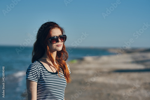 portrait of a beautiful traveler with glasses red hair t-shirt beach summer landscape sea © SHOTPRIME STUDIO